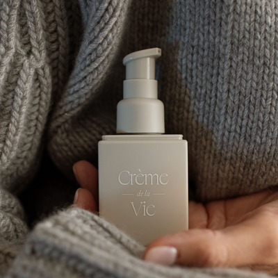 A picture of a woman's hand holding creme de la vie moisturizer over a knitted sweater