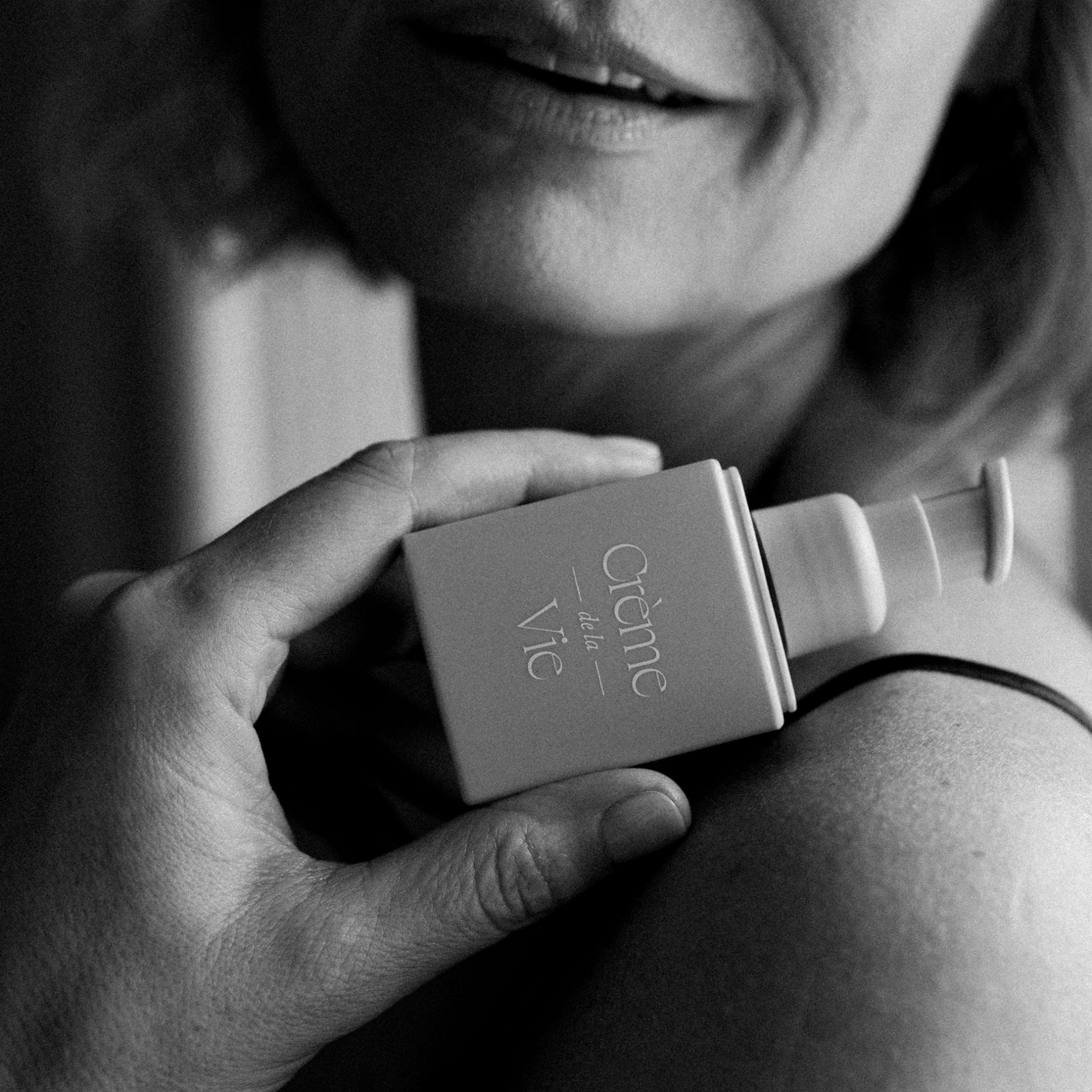 A black and white photo of a woman holding creme de la vie moisturizer on her shoulder and smiling