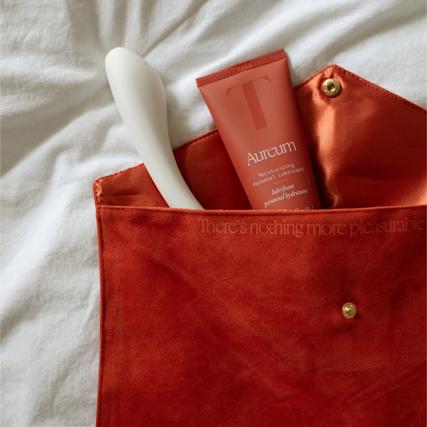 The Golden Hour pouch on a white sheet with the Nuri massager and Aureum personal lubricant sticking out of it